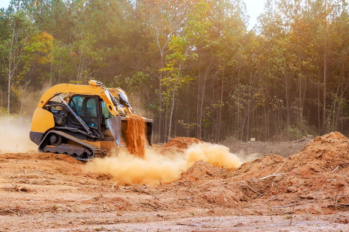 Skid steer clearing trees and moving soil on a forested jobsite
